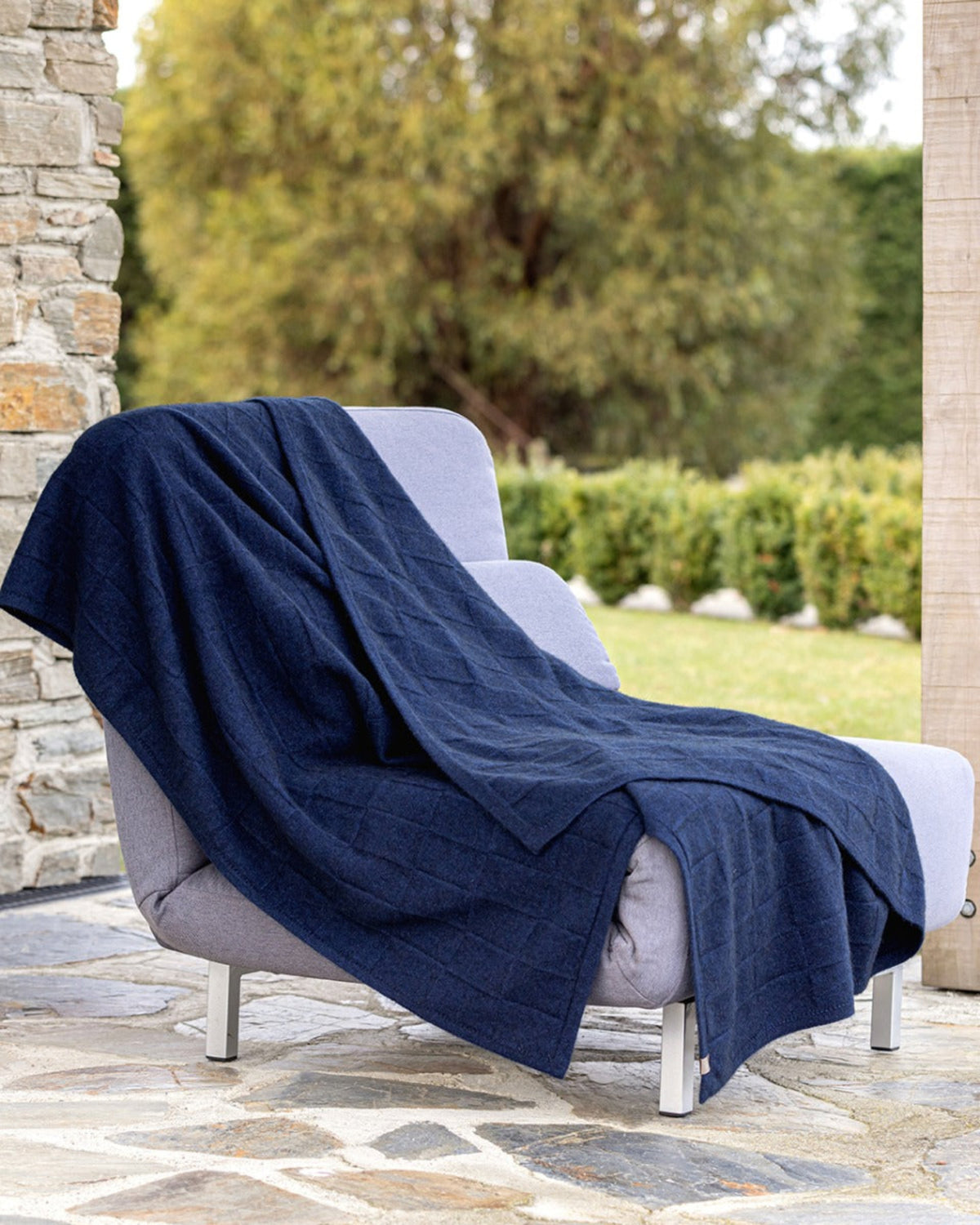 basket weave possum merino Navy blue blanket draped over a gray chair outdoors with greenery in the background