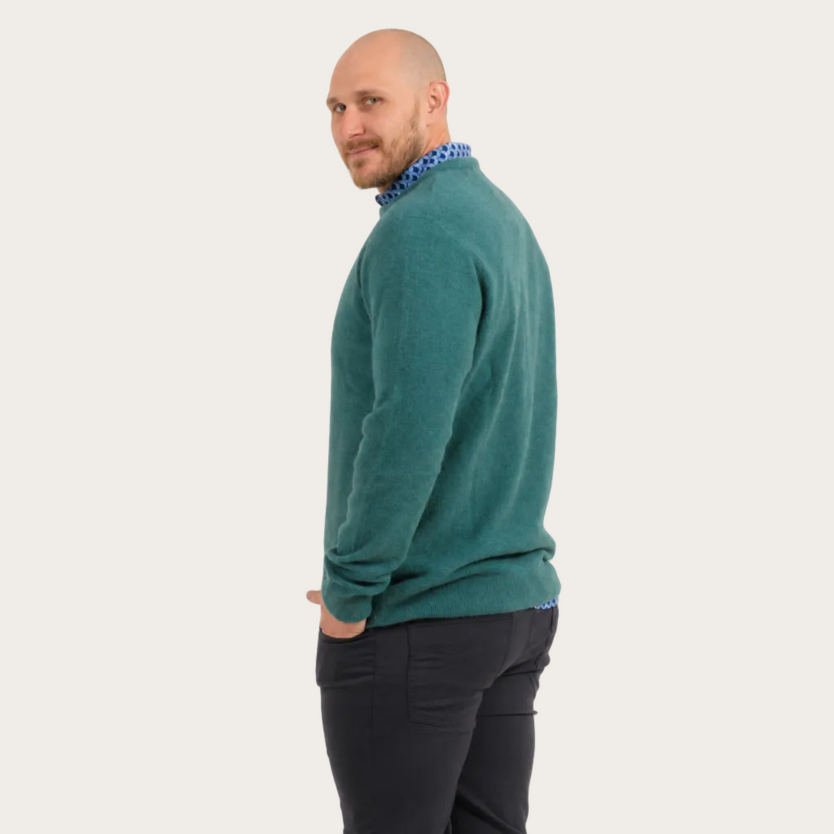 Man wearing a teal possum merino sweater and dark pants on a plain background