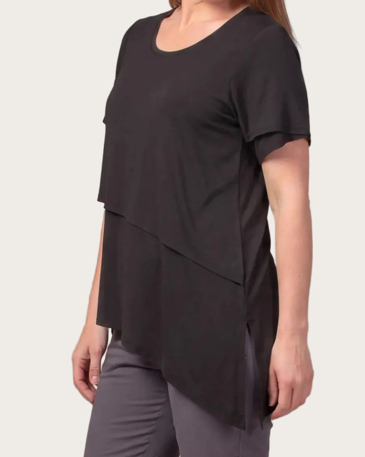 A woman wearing a black bamboo short-sleeve top with an asymmetrical layered hem, 