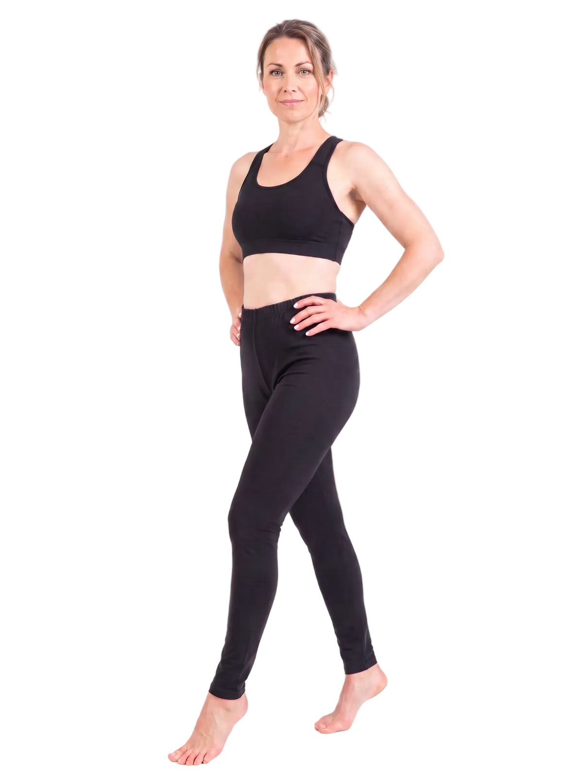 A woman modeling a black sports bra and matching black leggings against a solid beige studio background.