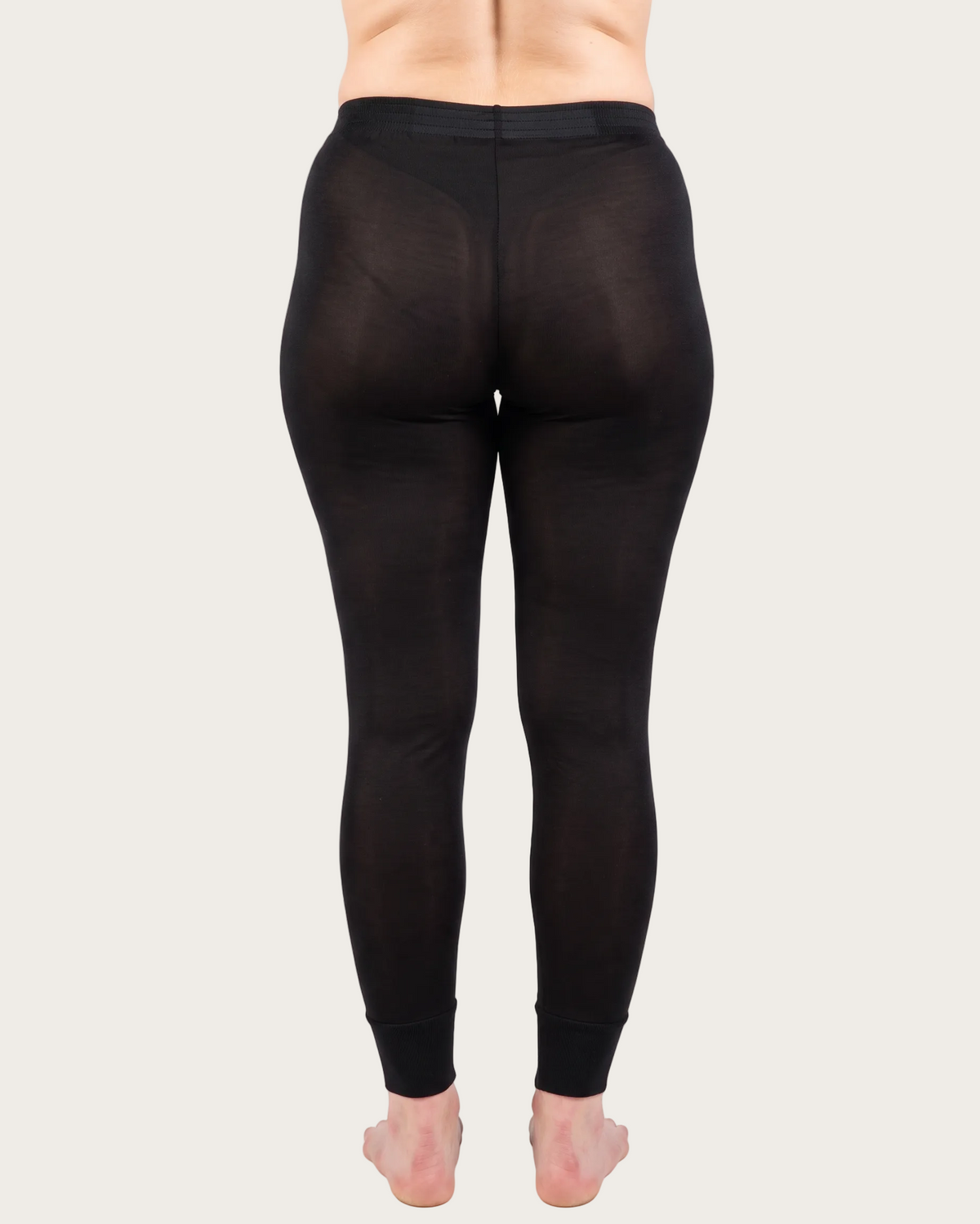 Rear view of a person wearing black full-length leggings against a plain white studio background.