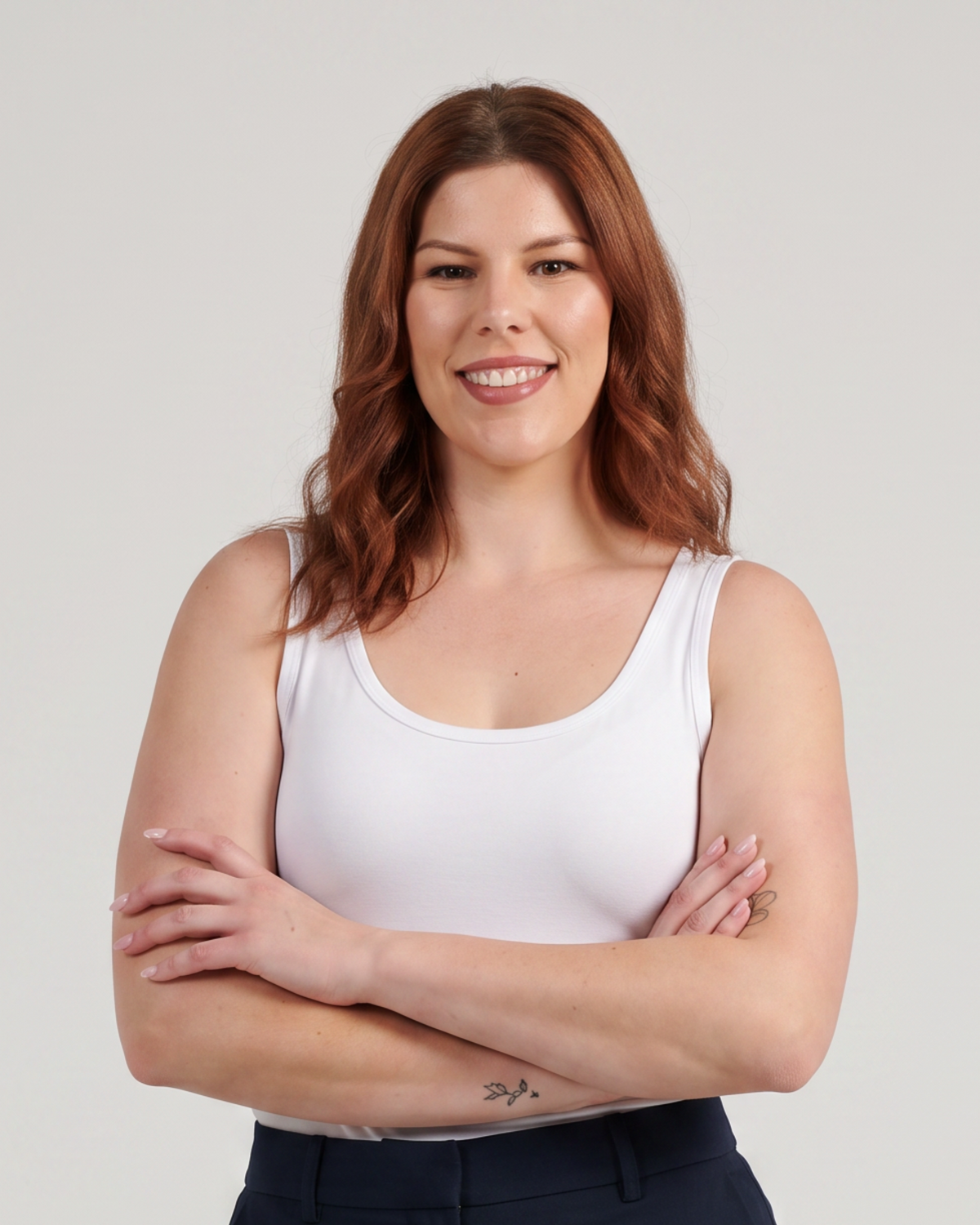 A woman modeling a pair of dark navy blue trousers with a white tank top, standing against a light gray studio background.