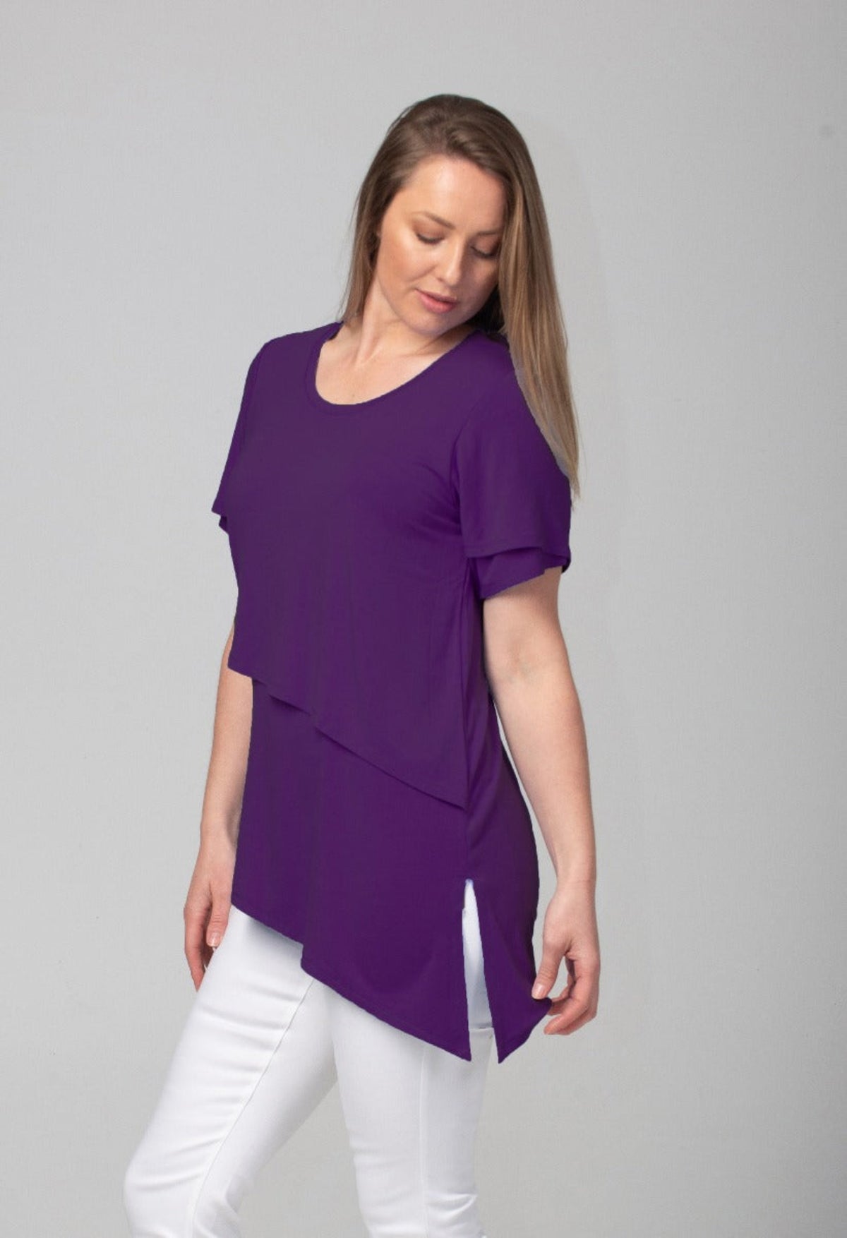 Woman wearing a bamboo purple layered top and white pants on a gray background