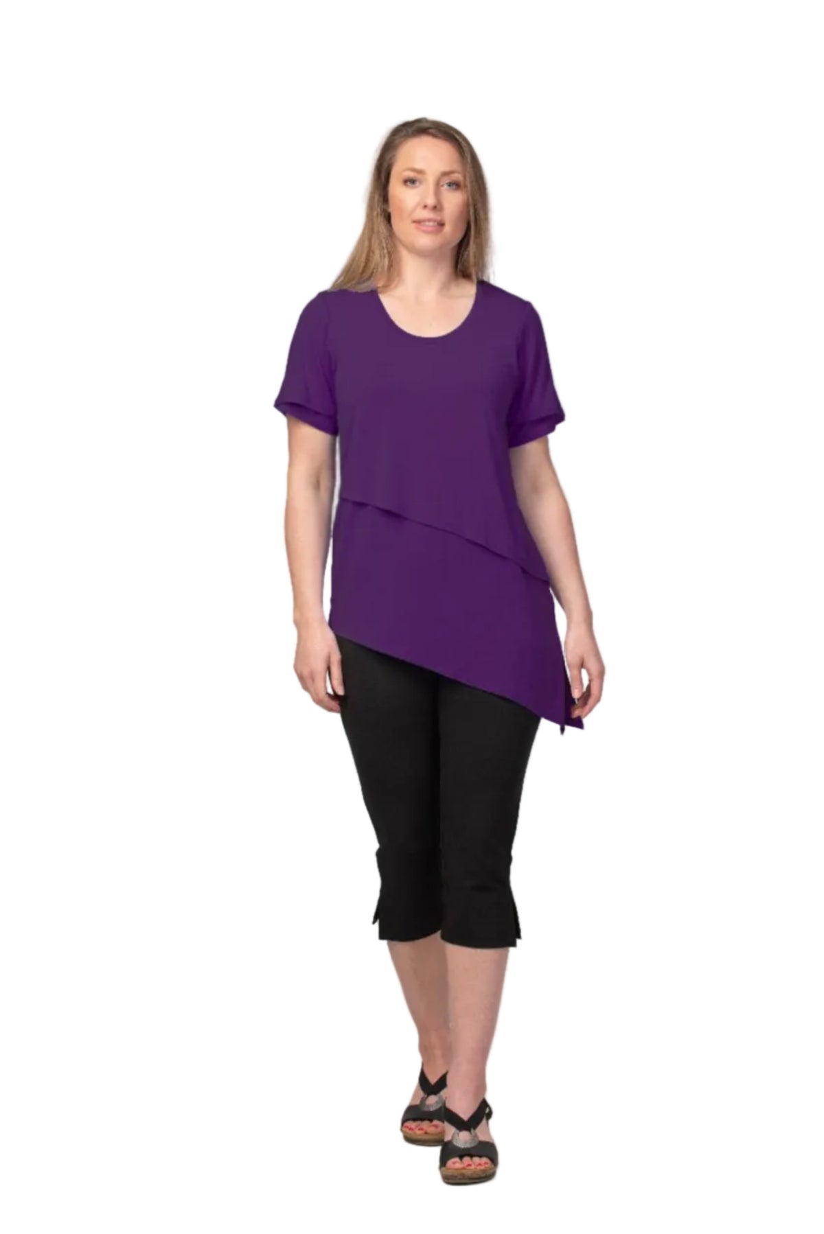 Woman wearing a purple layered top and black capri pants on a gray background
