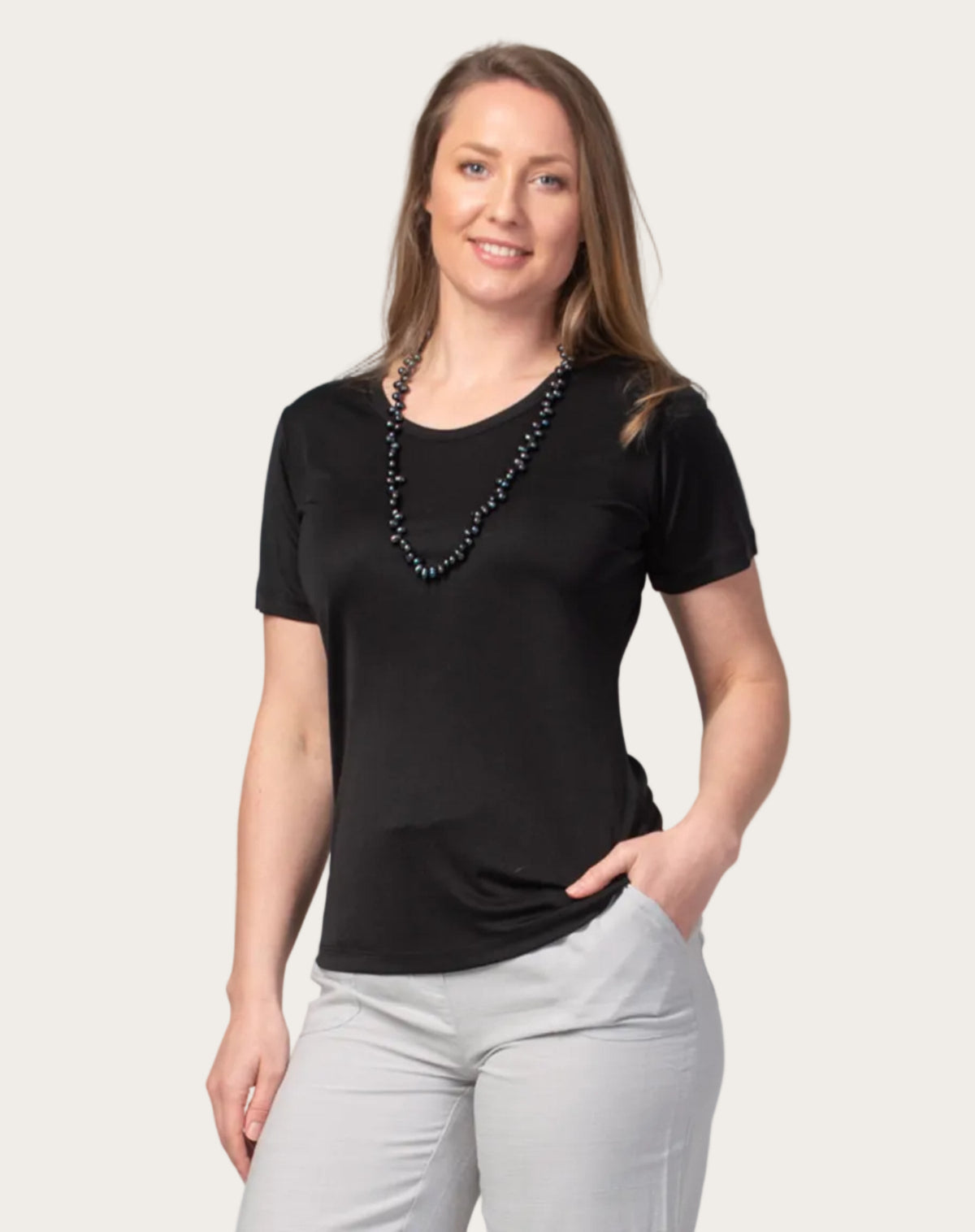 Woman wearing a silk black t-shirt and light gray pants against a gray background