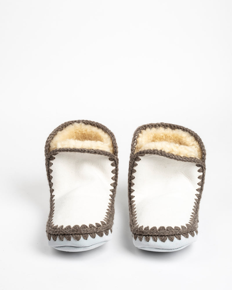 Pair of sheepskin slippers with brown trim and white sole on a light gray background